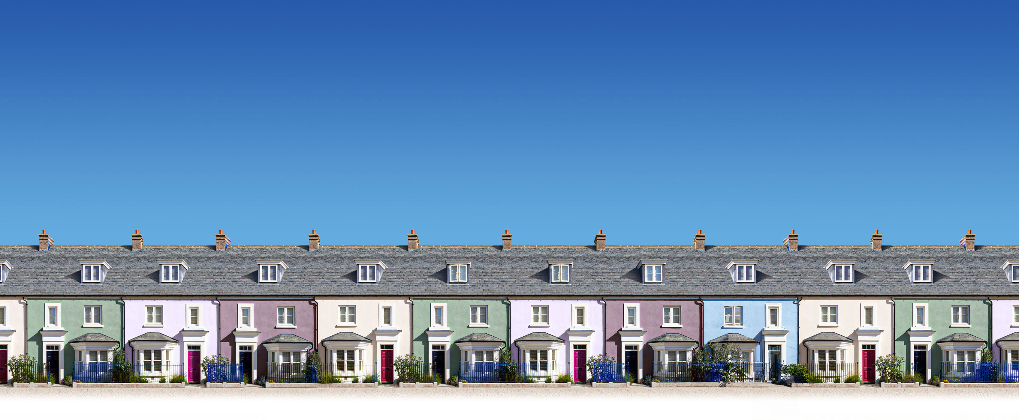 A row of pastel-colored terraced houses with gray slate roofs under a clear blue sky.